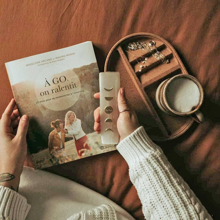 Deux mains qui tiennent le livre A go on ralentit et un cristal. / Two hands holding the book A go on ralentit and a crystal.